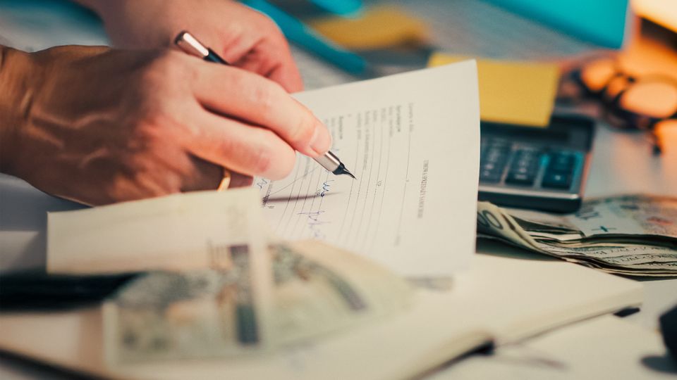 Assinatura de documentos ao lado de dinheiro e calculadora sobre a mesa